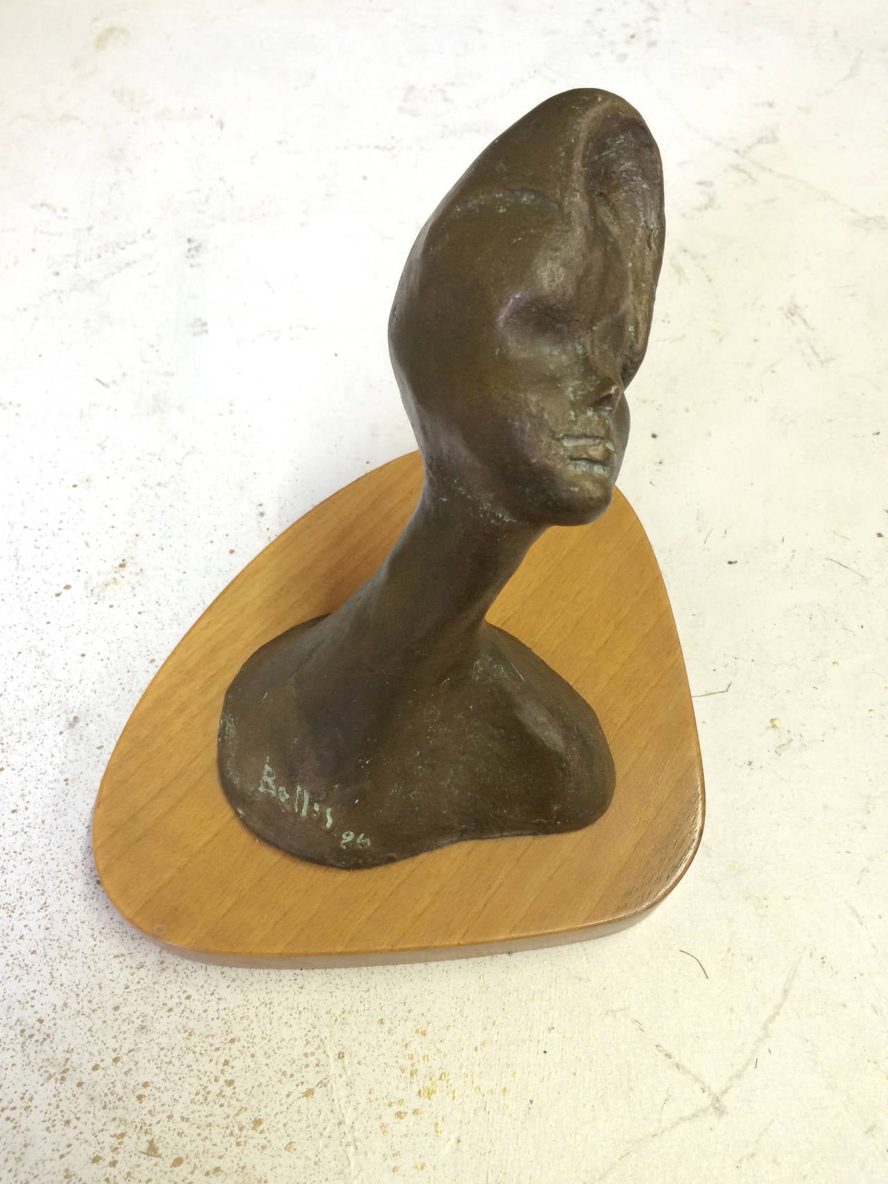 This sculpture of a woman's head with a giraffe-like neck is mounted on a slab of wood and is signed 