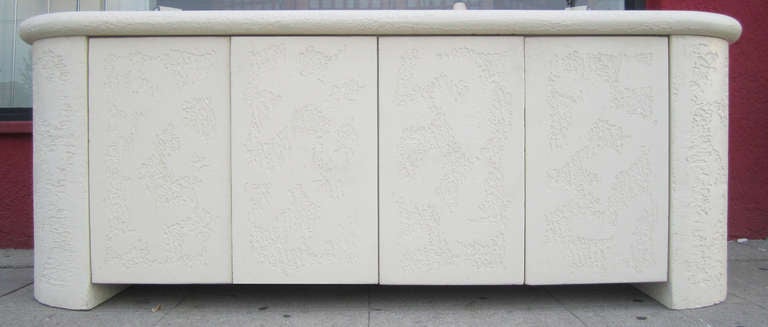 This striking credenza with rounded edges features a faux stone finish in textured plaster surmounted by a white washed wood top. The four doors open to reveal one shelf on each side.