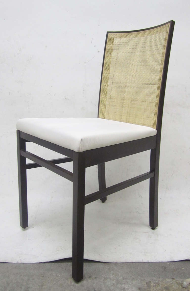 These handsome, Italian dining chairs feature a solid stained birch frames with light-colored, caned backs. The seats are upholstered in white vinyl.