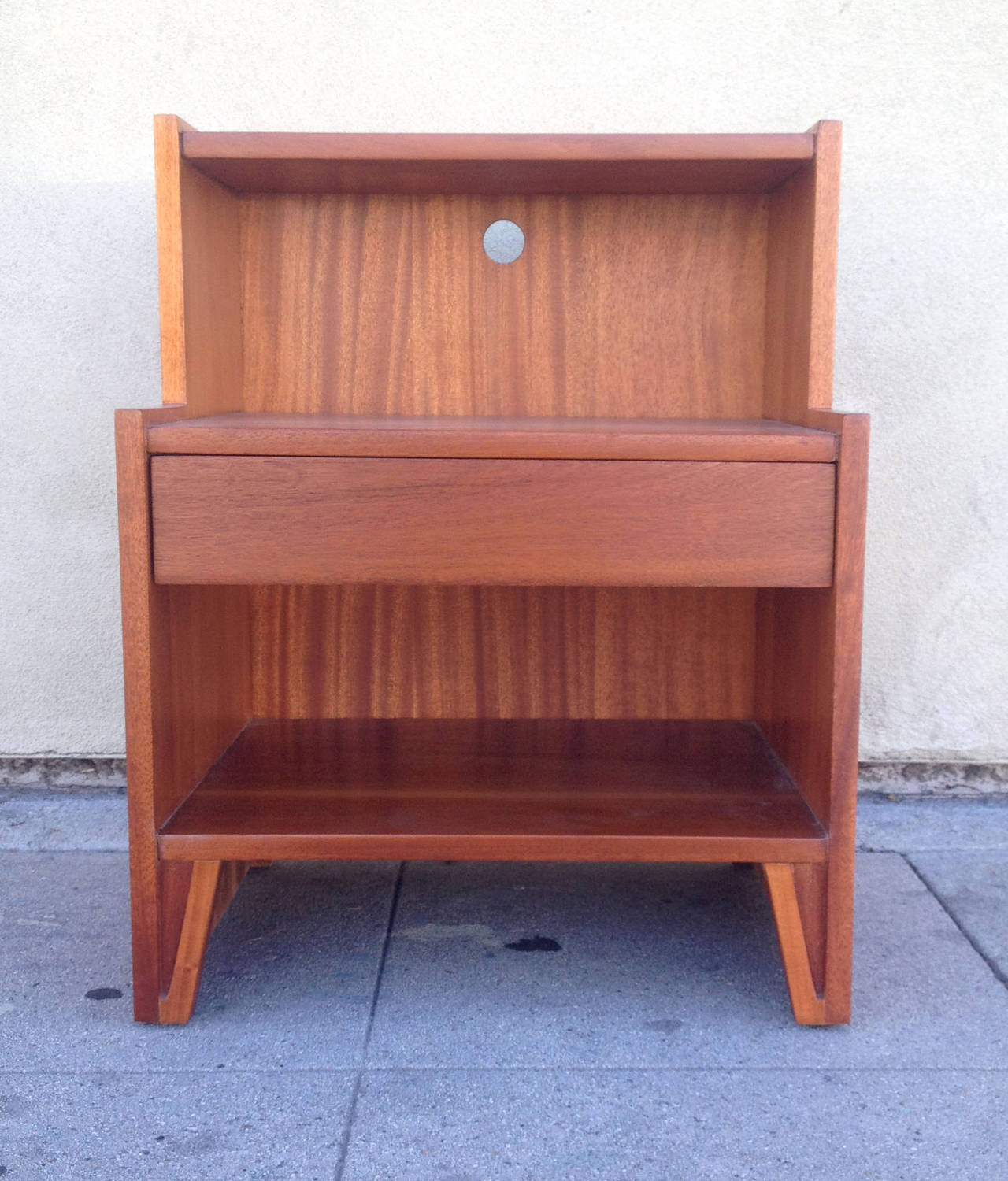 This pair of mid-century modern Landstrom nightstands features an architectural two-tier frame, rendered entirely in rich solid mahogany . The recessed top shelf is supported by a deeper bottom shelf with a single drawer in between. On the back