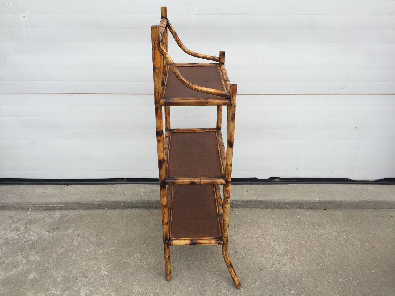 This scorched bamboo Etagere with bent legs has three different levels of shelving.  The shelves are lined with espresso painted Rattan and are ready to be filled with decorative goods.  Made in England and made in the 1930's.