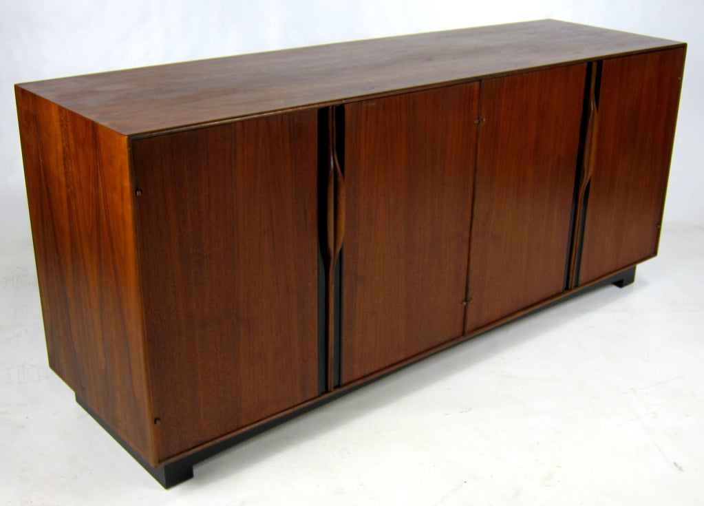 Fine walnut buffet cabinet with sculpted door handles on black enameled base by John Kapel for Glenn of CA. The interior is fitted with adjustable shelves and lined flatware drawers.