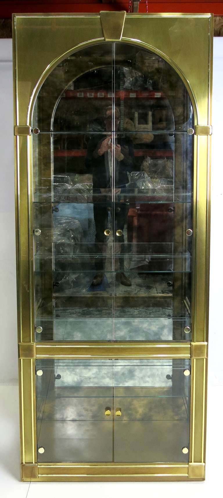 Fantastic Brass Clad Vitrine with Arched doors and Keystone pediment.  The lighted interior has five adjustable glass shelves with etched plate grooves and a dramatic smoked mirror back.  This example is in virtual mint condition with absolutely no