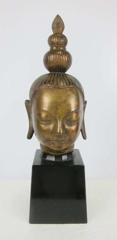 Finely cast bronze Buddha head mounted on a tall ebonized tapering wood base.