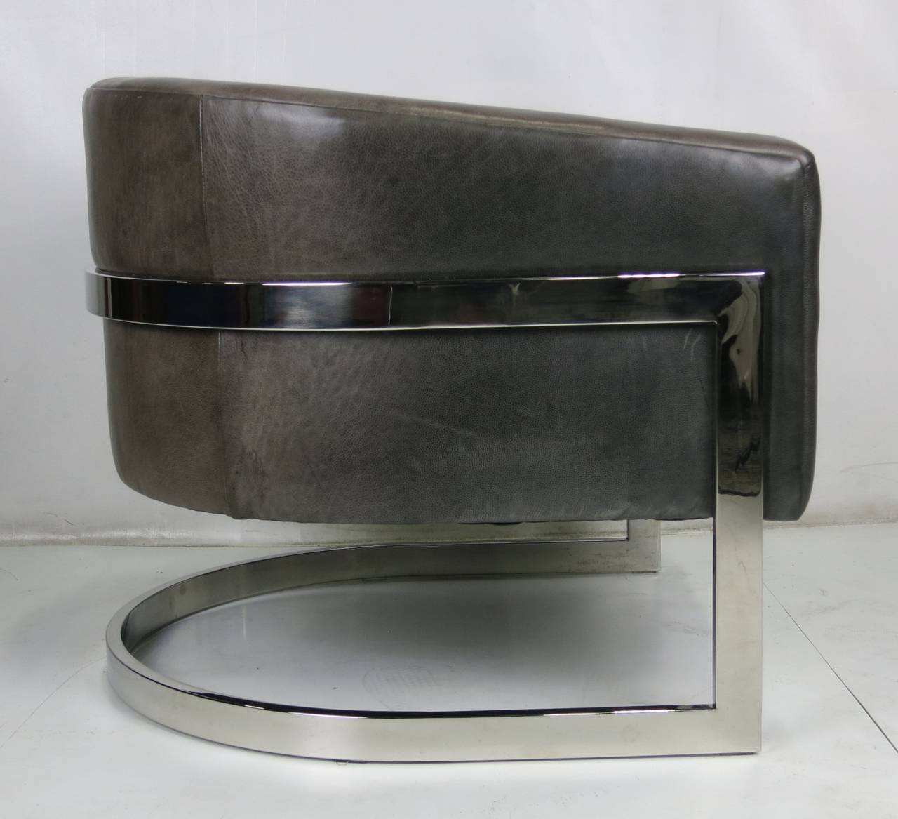Fantastic pair of large-scale barrel form lounge chairs with wraparound chrome frame by Milo Baughman. The chairs are in excellent condition, recently upholstered in charcoal grey top grain leather. The chrome frames have also been re-plated and are