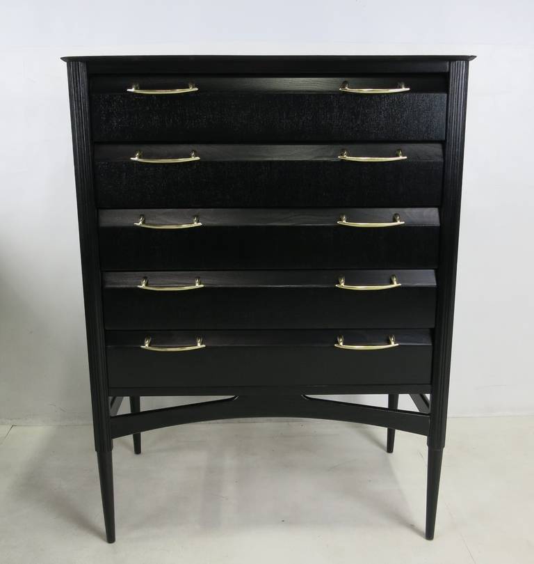 Ebonized mahogany tall dresser with polished brass pulls. The piece is raised on fluted stiletto legs with sculptural stretchers.