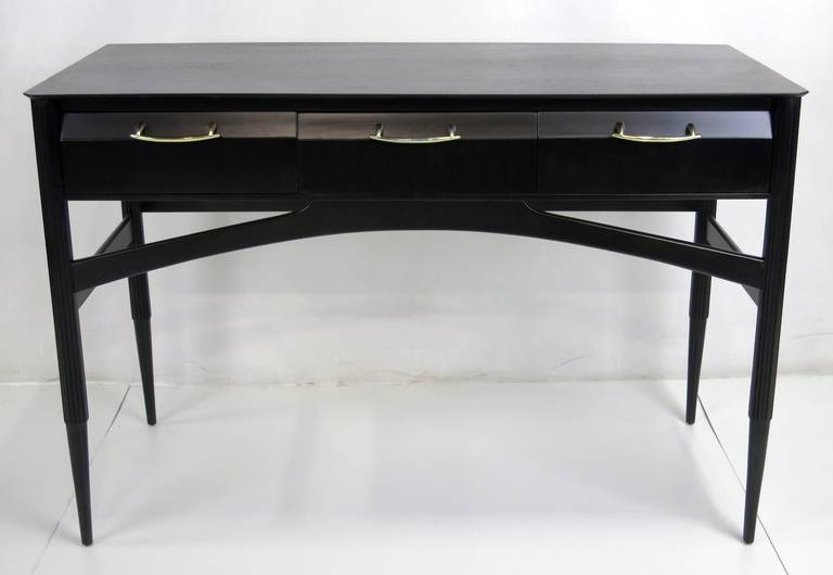 Ebonized mahogany writing desk or vanity with fluted stiletto legs and sculptural stretchers.  Polished and lacquered Brass drawer pulls.