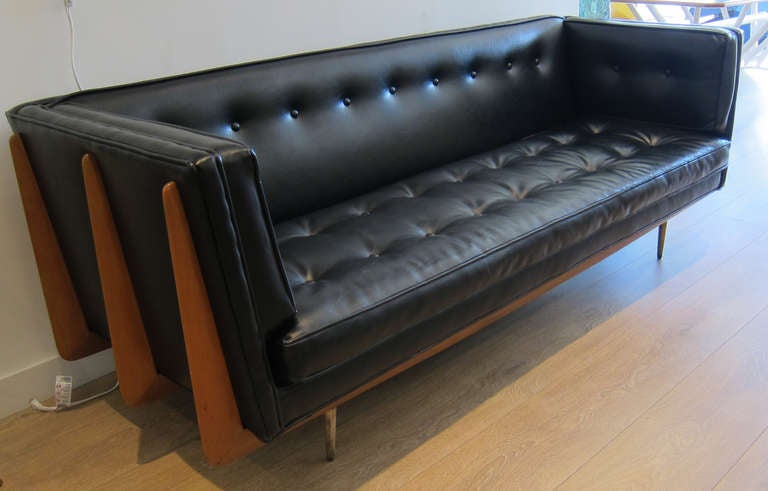 A modernist sculptural wood frame three seater sofa, original black simili leather, raised on brass fluted legs.
