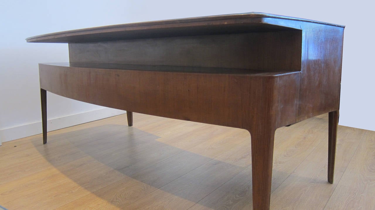 A rare late 1940s executive desk by Gio Ponti. Bowed rosewood desk featuring original inset green glass top, (signed Fontana Arte). Tapered legs, four locking drawers, open shelf.
Sold in as found original condition and could be restored upon