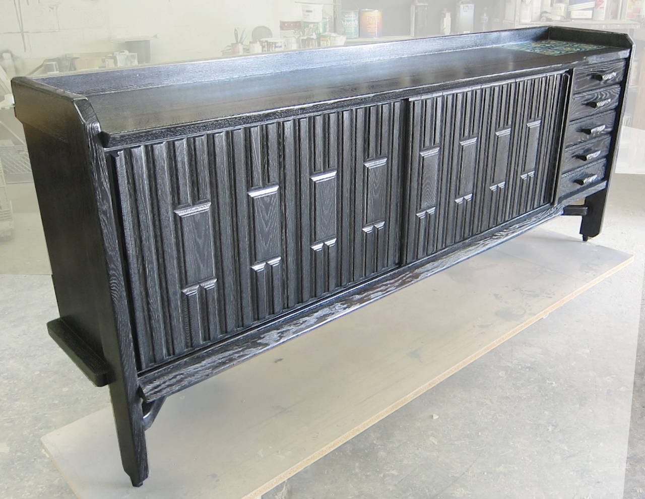 A French 1950s sideboard by Guillerme and Chambron for Votre Maison. Black cerused oak patina with ceramic tiles inlaid on top, two front sliding doors revealing fixed glass shelves on either side. Five drawers with black ceramic pulls.

.