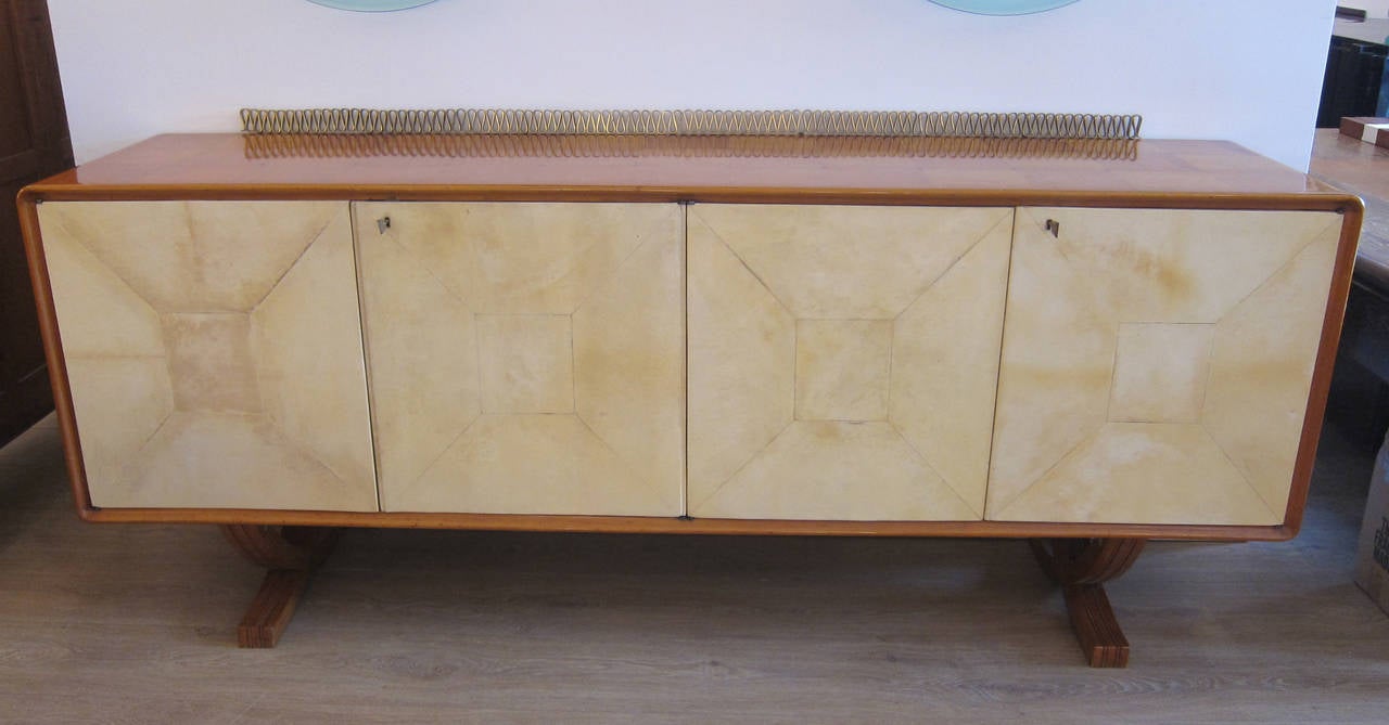 Rare fruitwood and parchment front sideboard, raised on two X-form bases. Parquetry veneered top with brass dot inlay, scrolling rear brass gallery. Four vellum wrapped doors with keys open to reveal a fixed shelf on either side.
By Paolo Buffa,