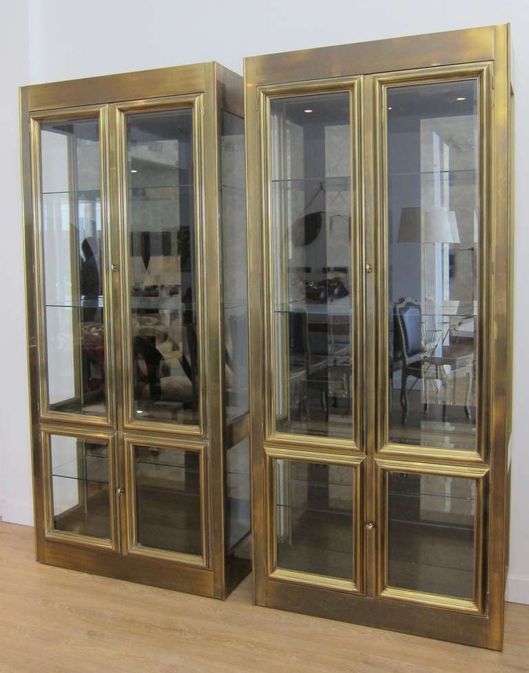 Pair of Mastercraft vitrines with mirrored back interior and  glass shelves. The vitrines are illuminated.  Great brass frame work  around the beveled glass doors.