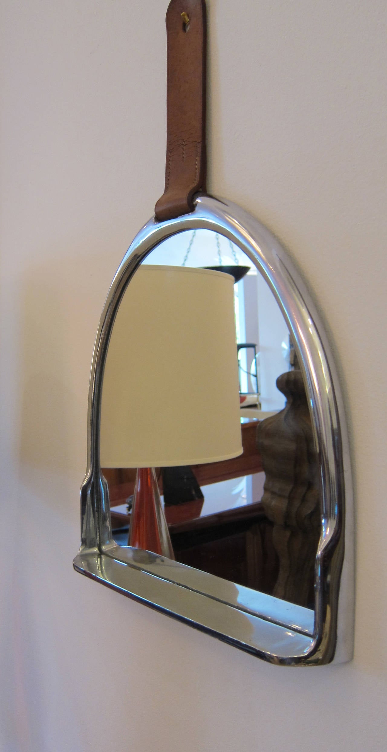 Chic chrome-plated stirrup shaped mirror with shelf and tobacco stitched leather strap, in the manner of Hermes or Gucci, unmarked.