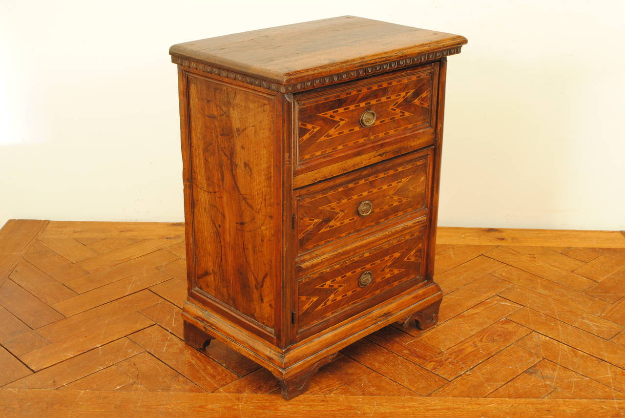 The rectangular top with a molded edge and carved lower gallery above one drawer and one door (converted from two lower drawers), the entire front of the cabinet nicely inlaid in geometric patterns with alternating colors of walnut, the pulls of a