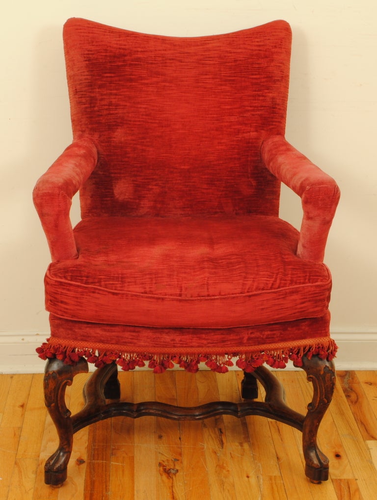 the curved backrest supported by upholstered arms and having a raised down cushion seat above a tassel lined bottom rail, the rear legs square and tapering are joined to the carved front legs by a curved stretcher, on raised carved feet