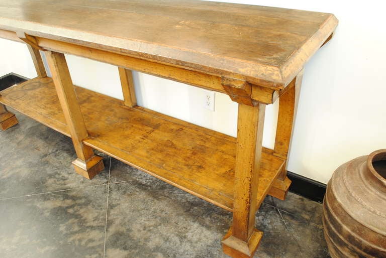 an interesting table having a rectangular top with beveled edges and vertical supports interrupting the apron, having six straight legs, the rear outside two with arched tops, having a bottom shelf connected to the legs which terminate into beveled