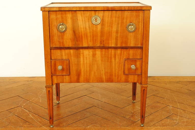 constructed of light walnut veneer, having a rectangular top with raised molded gallery edge above a conforming case with one large upper drawer and two smaller square drawers within the lower half, the sides having brass handles, raised on square