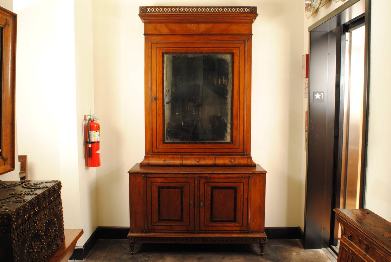 Of two-piece construction, the upper section having a pierced gallery and a large mirrored door, the interior covered in velvet, with three convex drawers also velvet lined, the bottom section with two doors and an interior upholstered in velvet,