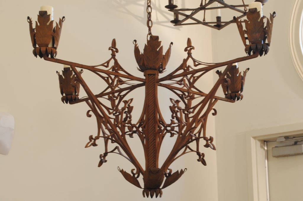 A very detailed wrought iron fixture with intricate fleurs-de-lis medallion designs flanking each of the diagonal arm supports and horizontal arms, the bobeches of large leaf-form metal, with ample chain and custom canopy.