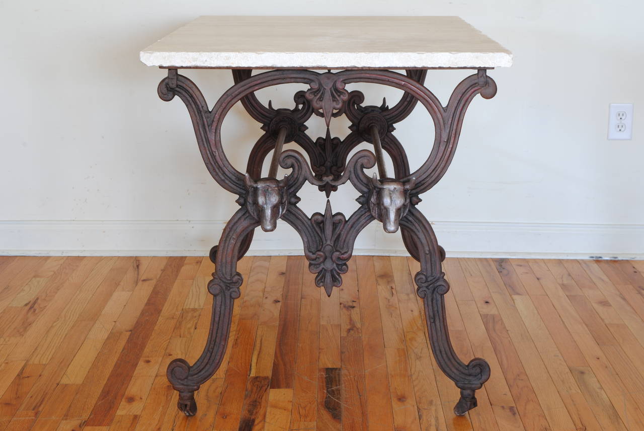 The later rectangular marble-top atop a table consisting of two trestle form sides connected by parallel rods, adorned with cast iron cows heads, raised on original casters.