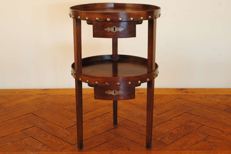 the round top and matching second tier each with wooden galleries attached by patinated brass nailheads, each level having a suspended drawer, the legs square, tapering legs going from top to bottom