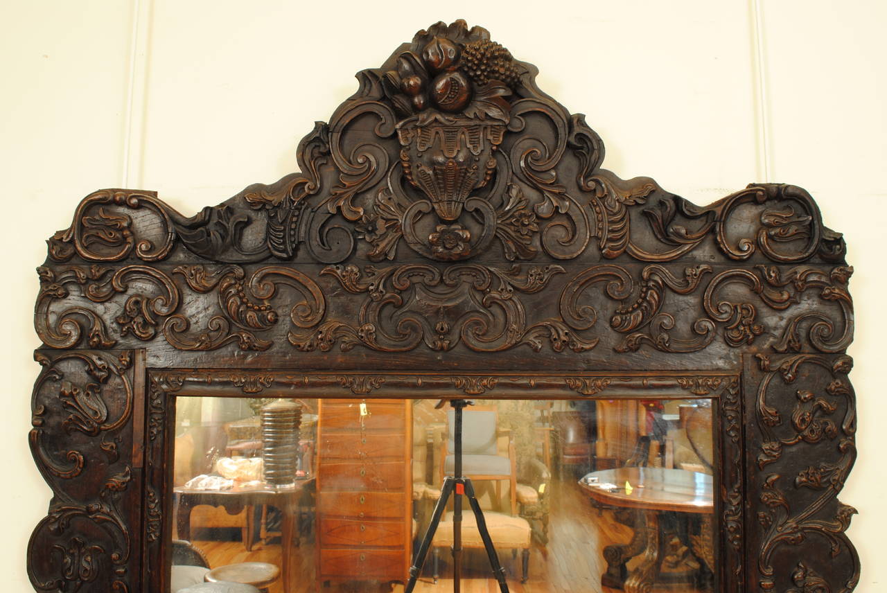 Probably composed of altar fragments, the carved frame constructed of elaborately carved panels of c-scrolls, flowers and shells, retaining an antique mirror plate.
