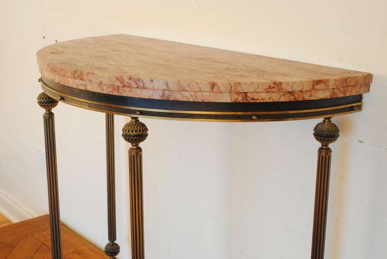 the two tier demilune shaped stepped variegated marble top, above a conforming frame of black metal and brass consisting of fluted columnar supports having pierced brass ball finial and terminals, the bottom having a shaped stretcher with decorative