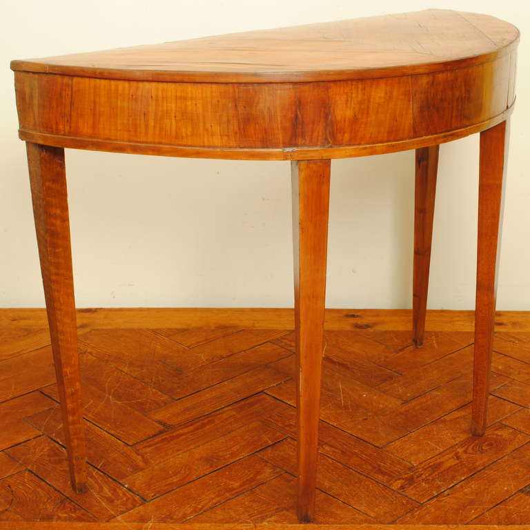 The demilune shaped top veneered in patterned walnut above a conforming apron, raised on square tapering legs.