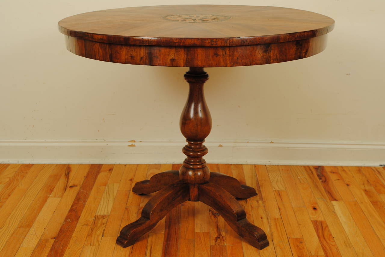 The circular top with radiating veneers and a central inlaid medallion, raised on a turned support and resting on a base of four shaped legs, 2nd quarter 19th century.