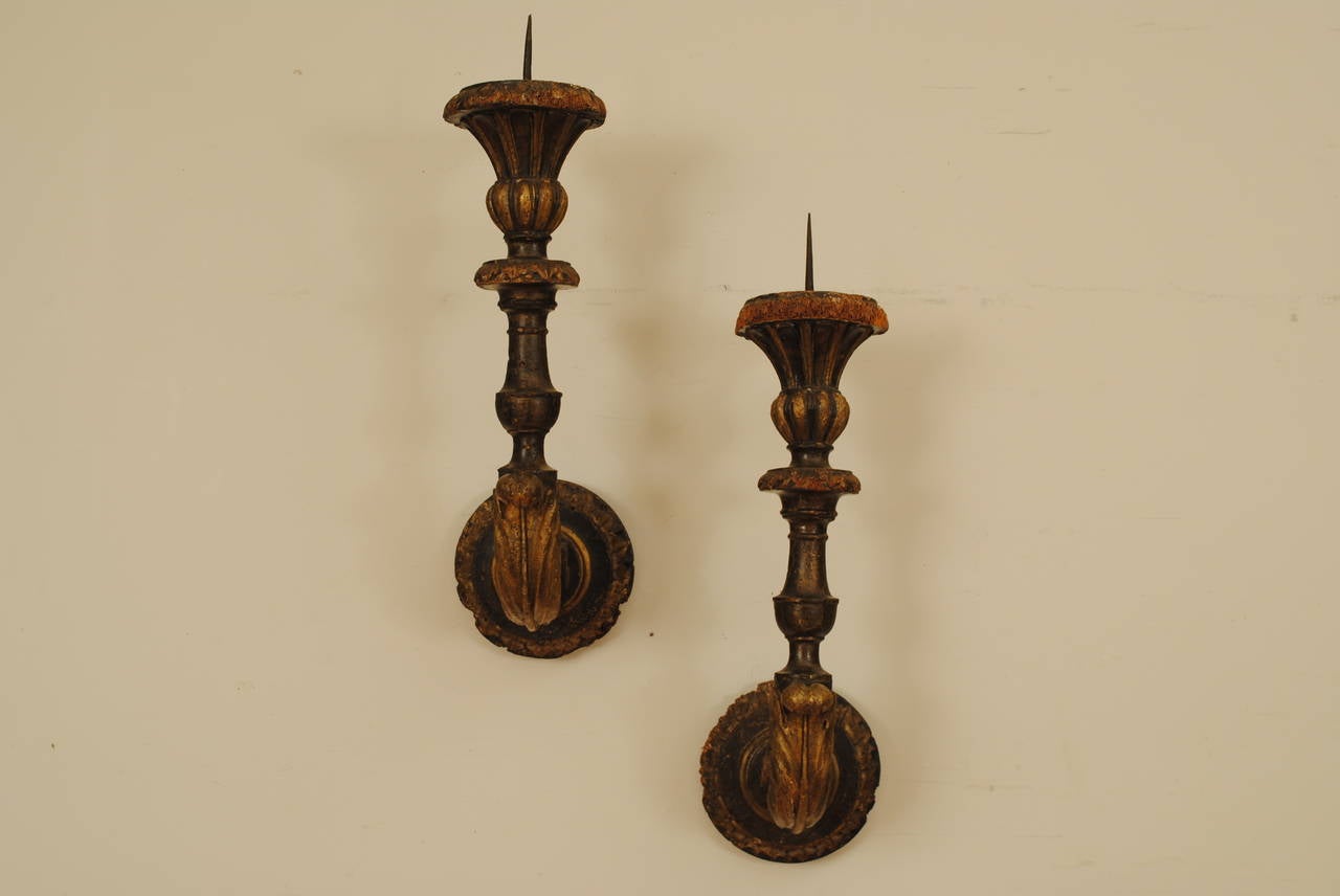 From Piacenza, Italy, 17th century, beautifully carved with circular backplates and a turned standard decorated with carved and gilded foliage, the fluted bobeches with original iron spikes.