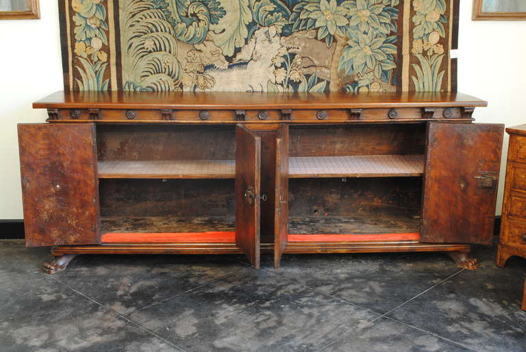 the single plank rectangular top above a conforming case adorned with carved details, the case having four doors among seven paneled sections, resting on a plinth form base and raised on carved paw feet