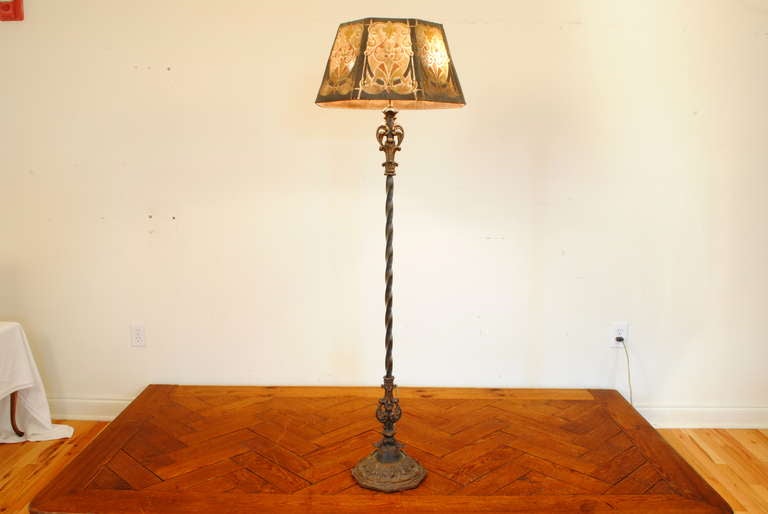 having an elaborately cast and painted iron base, the twisting iron standard continuing upward to a decorative iron finial, the lampshade of perforated metal and retaining its original painted pattern, diameter of base: 10 in.

Please go to