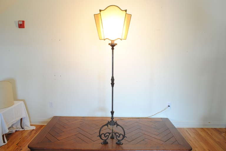 The shade trimmed in a fabric gimp, the floor lamp having a pierced bobeche and raised brass turnings at top, middle, and bottom where it meets a tripartite base with under scrolled legs and raised on flattened bracket feet, sold with shade 

