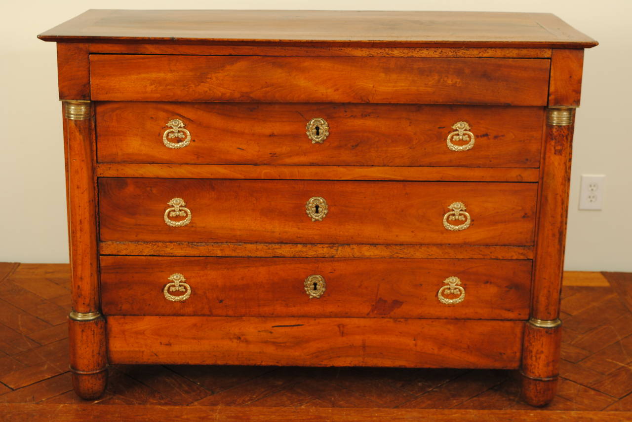 The rectangular top above a conforming case with one hidden upper drawer and three brass-mounted drawers flanked by columns mounted with brass hardware, paneled sides, raised on ovoid feet.