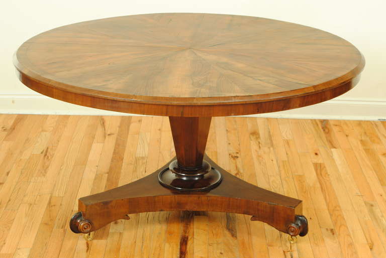 Beautifully veneered walnut top with apron, on tapered pedestal and tripartite base, the carved feet raised on castors