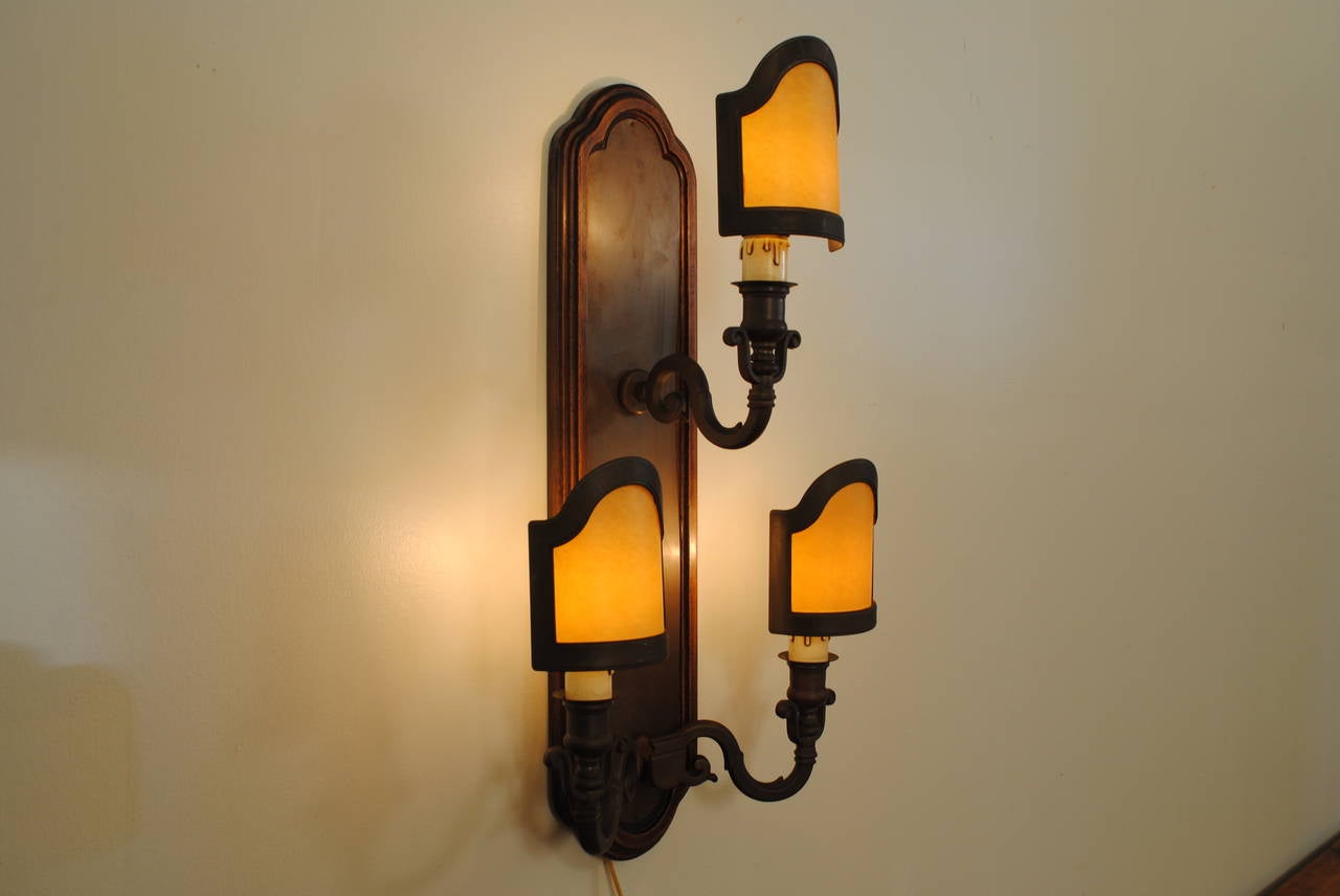 Set of five Italian Baroque style three-light wall sconces in patinated brass and wood. Having shaped wood backplates with brass surface, scrolling arms with original brass and parchment lampshade.