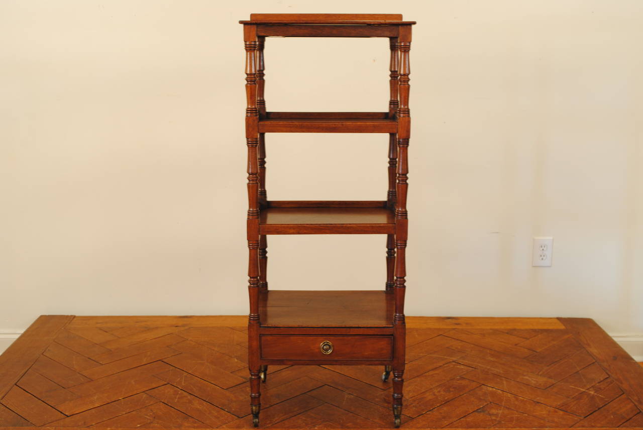 Having an adjustable top section with bookrest, each rectangular gallery tier connected by turned supports, the bottom section having one drawer, raised on turned feet ending in original brass casters.