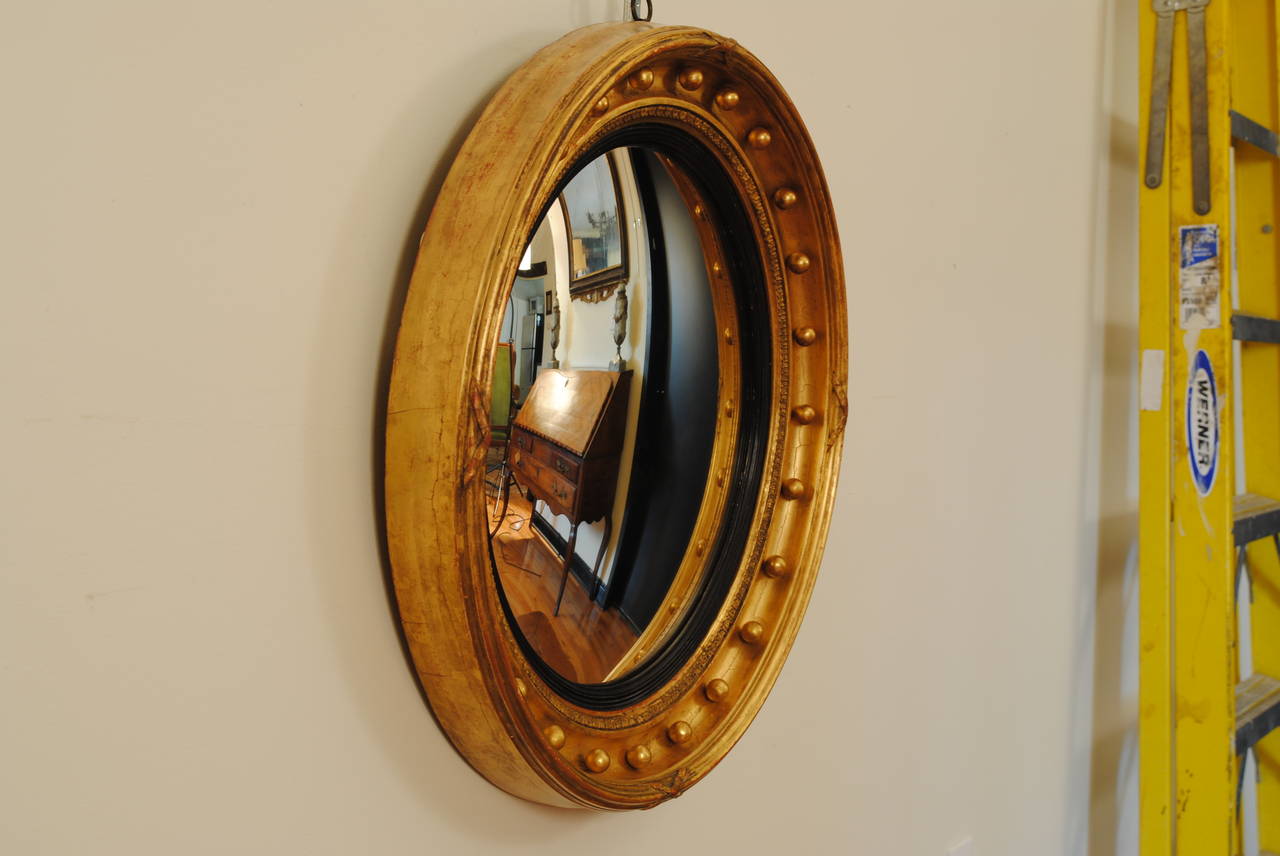 The round frame with a raised molded edge and carved ribbons, the inner convex section decorated with gilded spheres and having an ebonized molded rabbet.