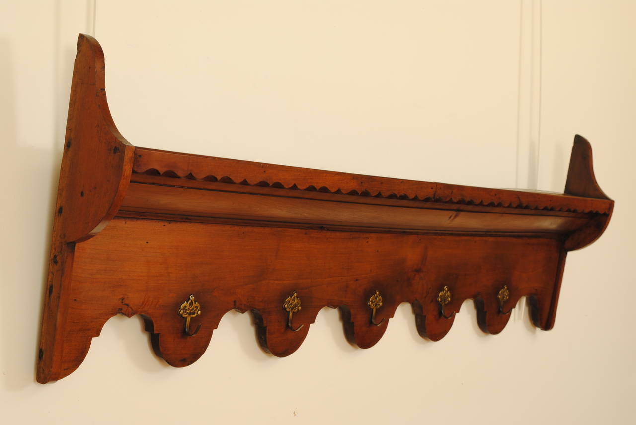 Having two shaped “wings” and a grooved upper plate shelf, the lower portion having shaped arches and each with decorative brass hooks.