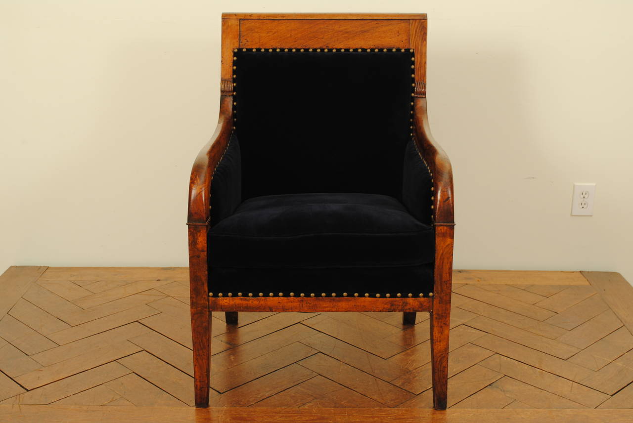 having a slightly overturned crestrail and downswept arms continuing to a flared sabre leg, the rear legs the reverse, generous down filled seat, the panels newly upholstered in dark blue velvet and trimmed in brass nailheads