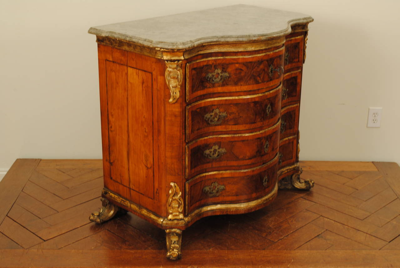 having its original marble top of serpentine form, the case housing 4-drawers each with a functioning spring lock requiring a key to open, with brass pulls and escutcheons, the upper case decorated with a stenciled giltwood trim and stylized rococo