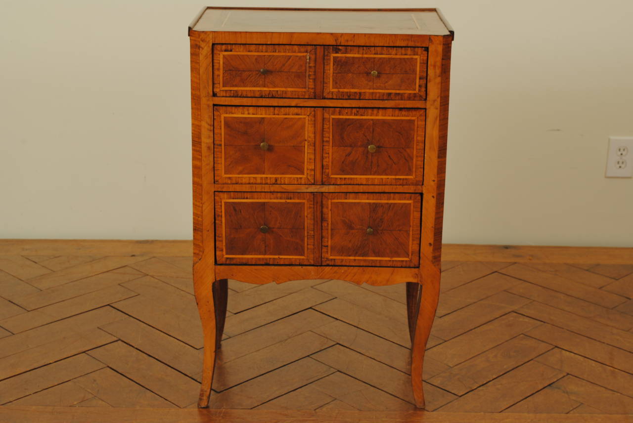 the rectangular top veneered and inlaid with various woods of banding having canted front corners and a raised gallery, the case housing three drawers with diagonally opposing veneers, the pattern repeating in a larger scale on the sides, raised on