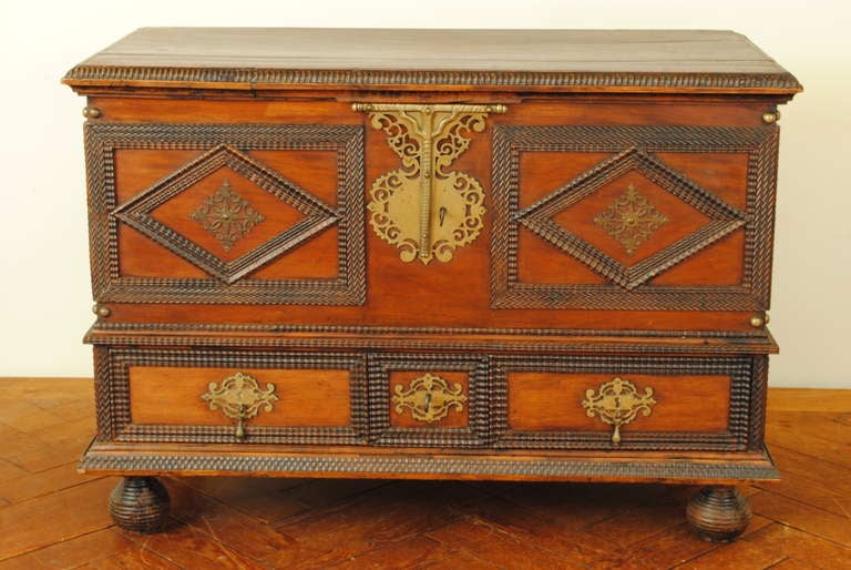 having a rectangular top with a carved molded edge above a conforming case patterned with carved lozenges within raised carved panels, and having a lower section of raised carved panels and brass hardware, both the top and bottom sections having