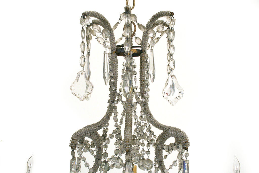 the scrolling iron framework wrapped completely in hand-strung micro-bead chain, the arms and gilt metal bobeches joined by swags of larger bead chains and hanging prisms