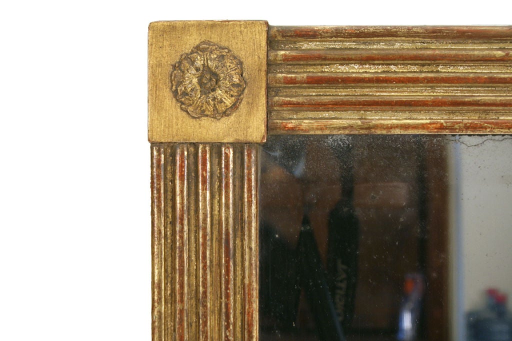 the rectangular frame having corner carved gilt-gesso corners on a square ground connected by reed carved giltwood sides, retaining original beveled mirrorplate