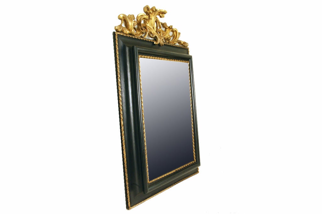 having a detailed foliate scroll giltwood finial atop a convex molded edge ebonized frame, the outer and inner borders trimmed in a braid carved giltwood, retaining the original beveled mirrorplate