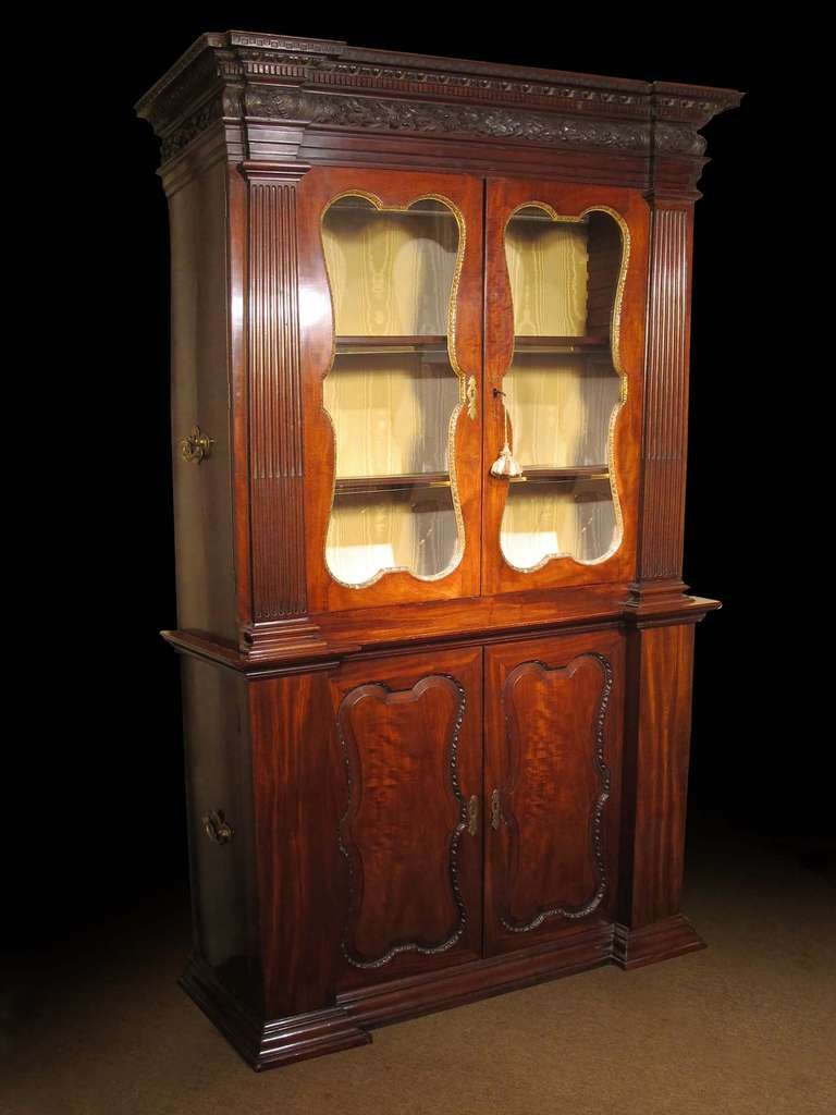 # A505 Fine early Georgian bookcase cabinet in the Palladian architectural taste. Executed in richly figured mahogany and enhanced with carved details including the stepped and carved cornice molding above a pair of doors with shaped glass panels