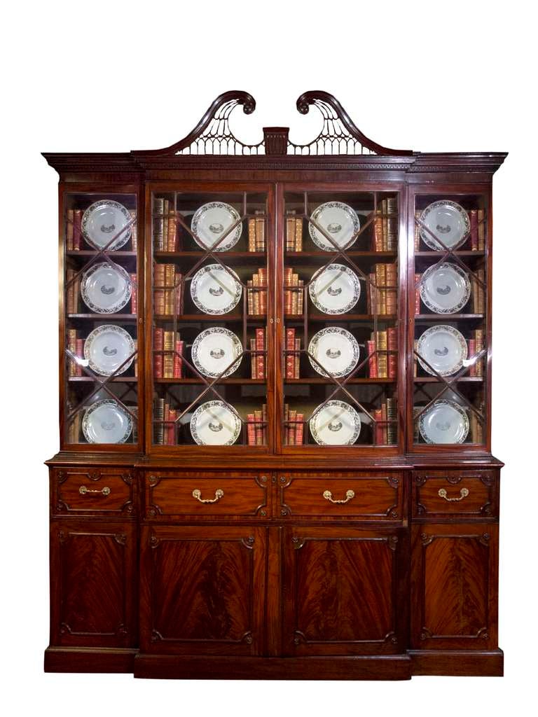 # V125 - Refined George III breakfront bookcase executed in mahogany and enriched with carved details and moldings. The detailed molded cornice centering a swan neck pierced fret work pediment. The upper section with glazed doors all with a