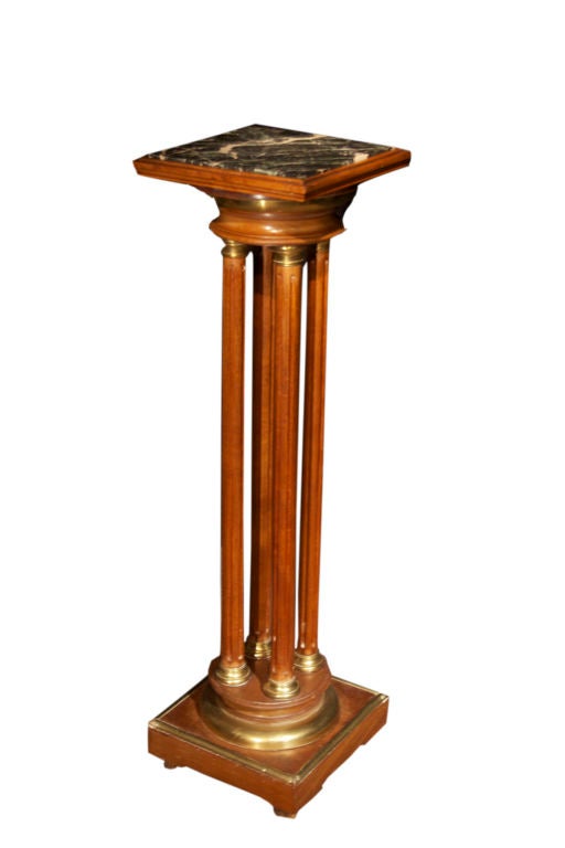 # W026 - French Directoire style pedestal executed in mahogany and enriched with brass details. The square inset veined marble top (with old repairs) supported on a round capital and raised on four fluted columns ending in a round base and square