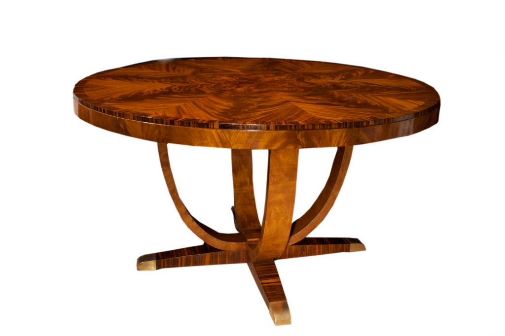 Art Deco circular dining table embellished with triangular panels of mahogany veneer with macassar framing, raised on four curved supports and four bar feet.<br />
Circa 1930<br />
<br />
<br />
See similar examples of center tables, dining